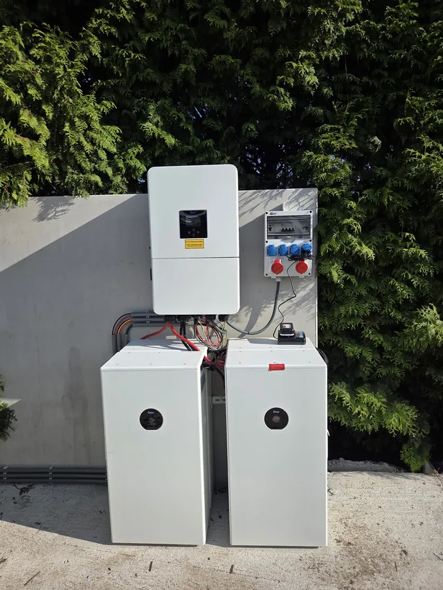 Deye inverter and CEE socket box outside on a concrete wall in front of a hedge, with two battery modules below.