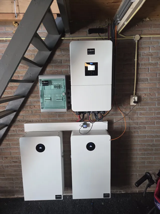 Deye inverter and distribution box on a brick wall under the stairs, with two battery modules below.