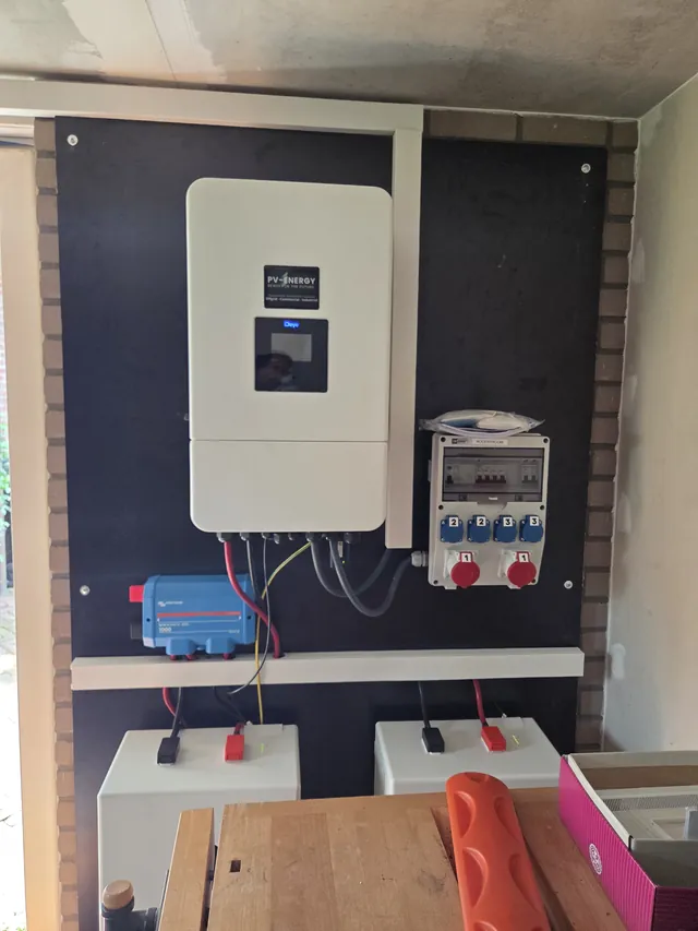 Deye inverter on a black board in a workshop, with CEE sockets and two battery modules below.