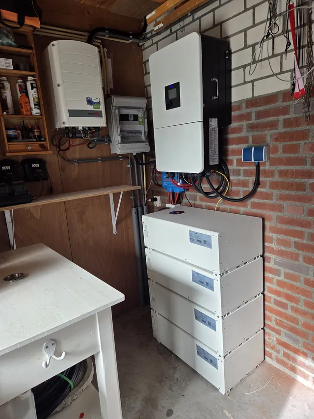Inverter next to a SolarEdge inverter in a garage, with a stack of four battery modules.
