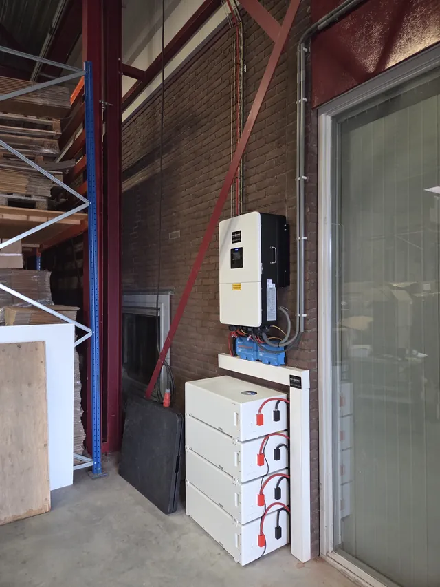 Deye inverter on a brick wall in a commercial unit, with a stack of four battery modules.