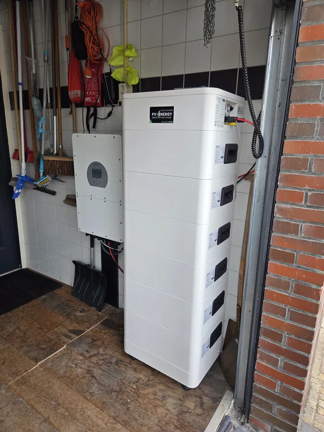 Deye inverter in a tiled garage next to a tall stack of battery modules.